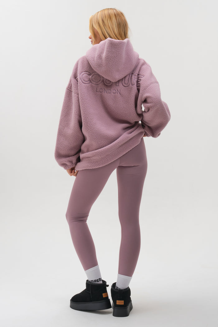 A person faces away, wearing the Isla Sherpa Hoodie & Leggings Set in mauve with LONDON embroidered on the back, black ankle boots, and white socks, set against a plain light background.