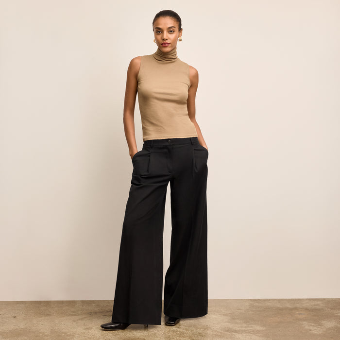 Woman wearing a beige sleeveless top and black wide-leg pants against a beige background