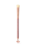 A makeup brush with a rose gold handle, a textured pink glitter grip, and a dangling bow charm at the bottom, shown on a clean white background.