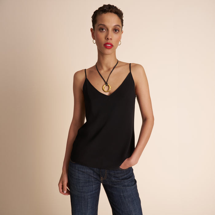 Woman wearing a black tank top and blue jeans against a beige background Lead