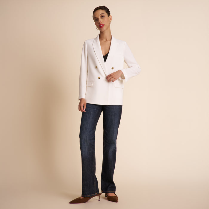 Woman wearing a white blazer and dark blue jeans on a beige background | Exclude
