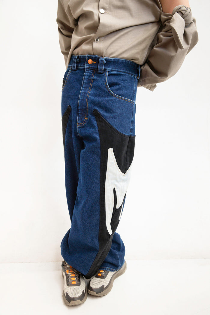 MANCANDY Rider M Jeans in stone-washed blue denim featuring contrasting black M-shaped side panels and a relaxed baggy silhouette.