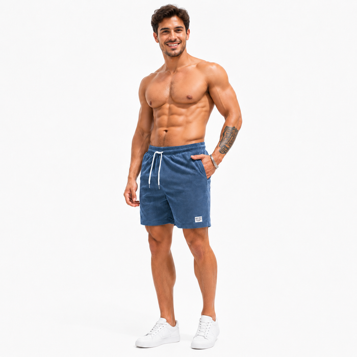 Men's blue corduroy drawstring shorts shown full length on a male model with white sneakers on a white studio background.