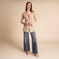 Woman wearing a beige blazer over a light blue shirt and jeans on a plain background | Lead