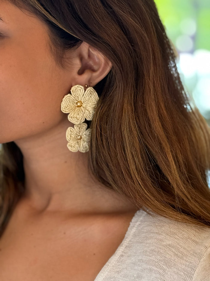 Dangly tan floral earrings being worn.