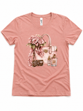 Soft pink short sleeve graphic tee featuring a handbag, floral bouquet, and glam accessory illustration.