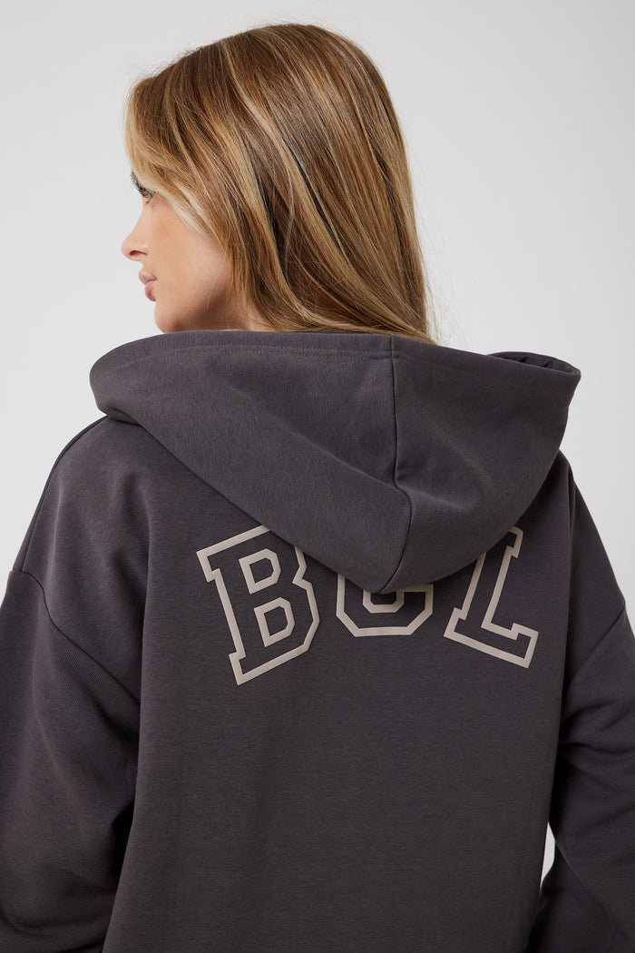 A woman with light brown hair is shown from the side and back, wearing the Ralph Street Wide Leg Tracksuit in Grey/Mocha, featuring a dark gray athleisure hoodie with large white-outlined "BCL" text on the back.