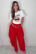 Bright red wide leg pants with a gathered elastic waistband, hand pockets, and a gold leaf chain detail at the waist.