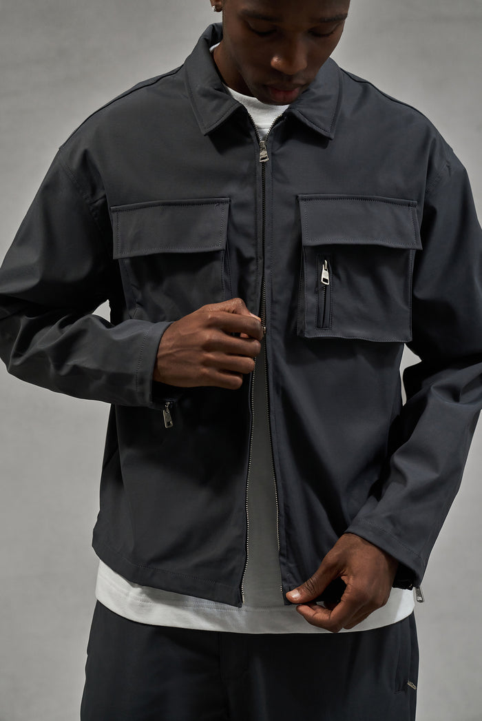 Close up image of a man wearing a long sleeve grey shirt and matching pants against a plain background.