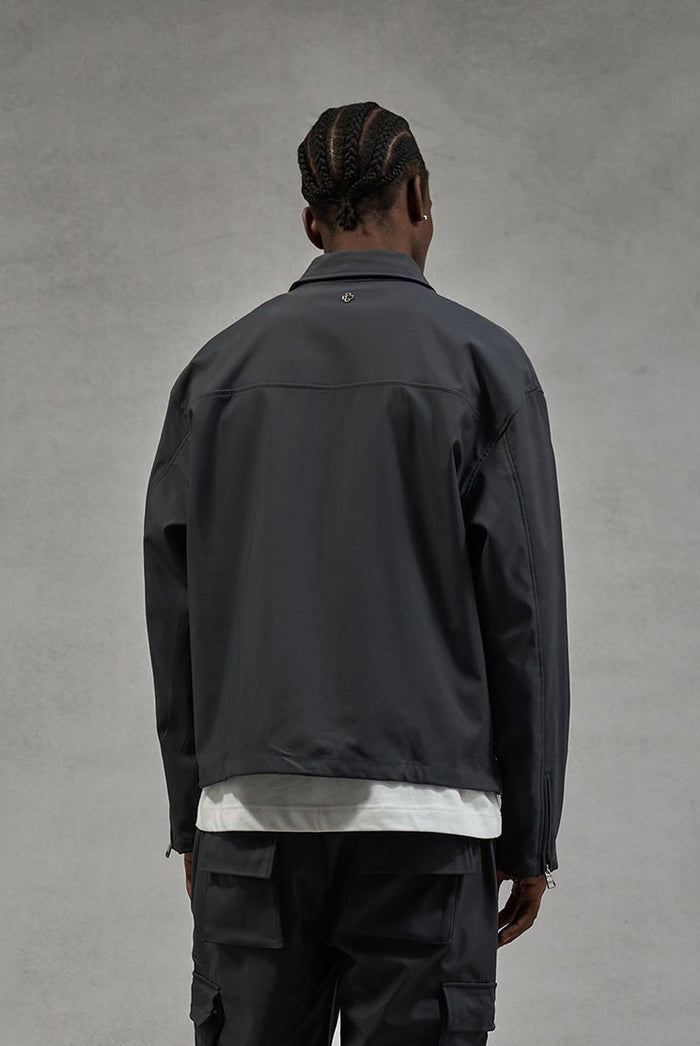 A person wearing a dark jacket and pants against a dark grey background.
