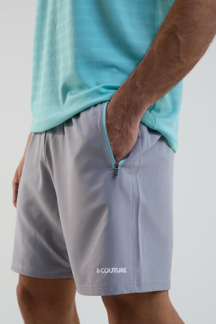Person wearing gray shorts with a brand logo on a plain background