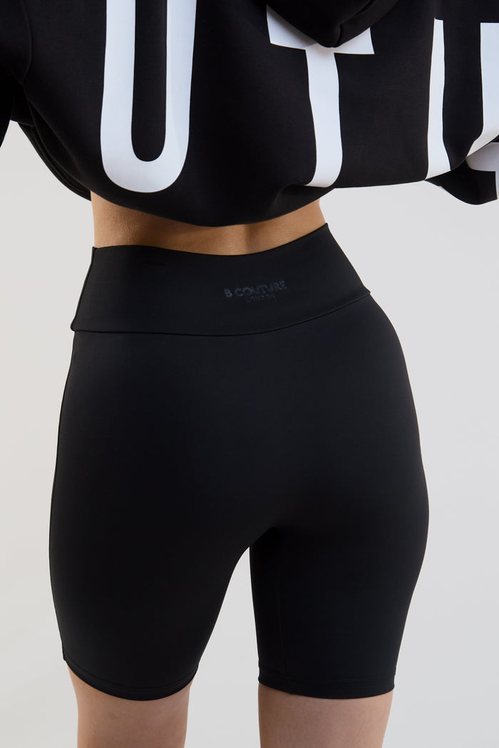 Person wearing black high-waisted shorts with a brand logo on a light gray background