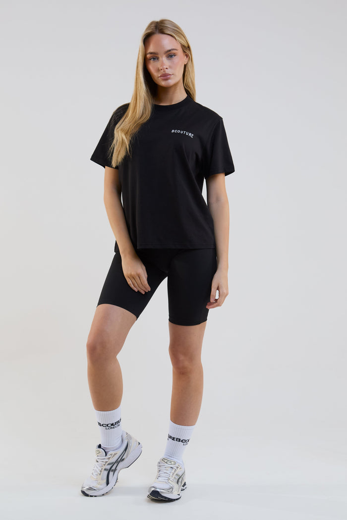 Woman wearing a black t-shirt and shorts with visible branding on a white background