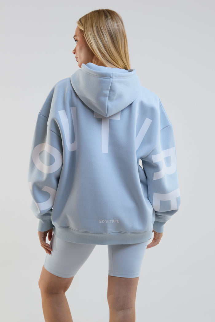Person wearing a light blue hoodie with branding on the back against a plain background
