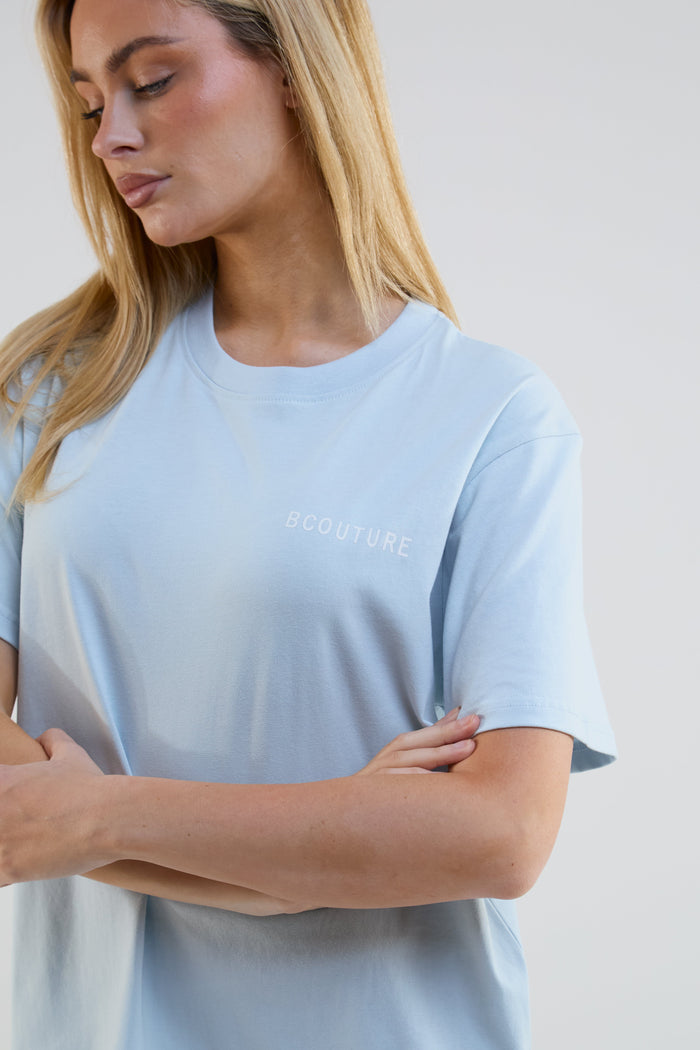 Woman wearing a light blue t-shirt with 'B COUTURE' branding on a plain background