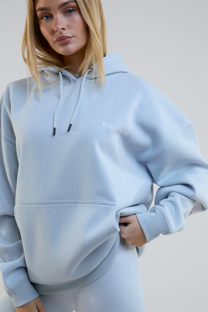 Person wearing a light blue hoodie with a brand logo on a plain background