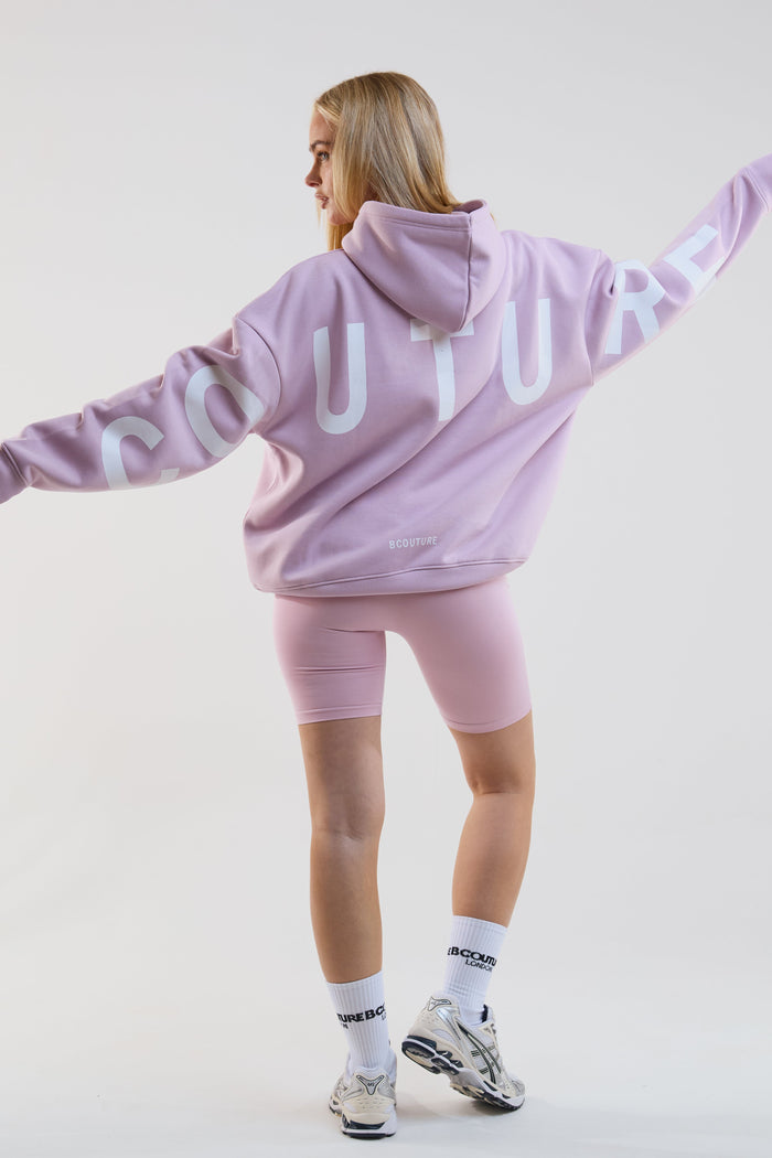 Person wearing a pink 'Culture' hoodie and shorts on a white background