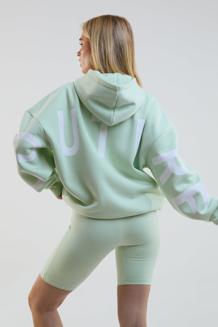 Person wearing a light green hoodie and shorts set with 'Vita' branding on a plain background