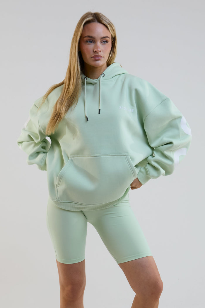 Woman wearing a light green hoodie and shorts set on a plain background