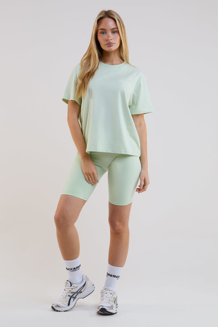 Woman wearing a light green outfit with shorts and a t-shirt on a white background