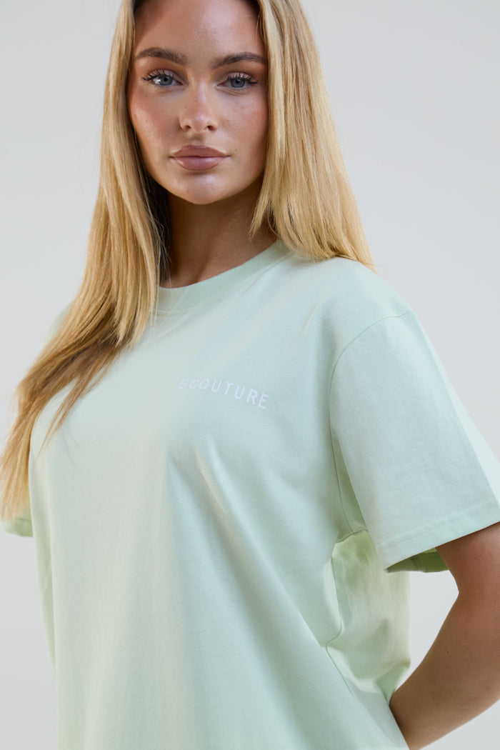Woman wearing a light green t-shirt with text on a plain background