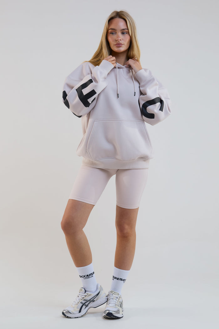 Woman wearing a light gray hoodie, shorts, and socks with a brand logo on a white background