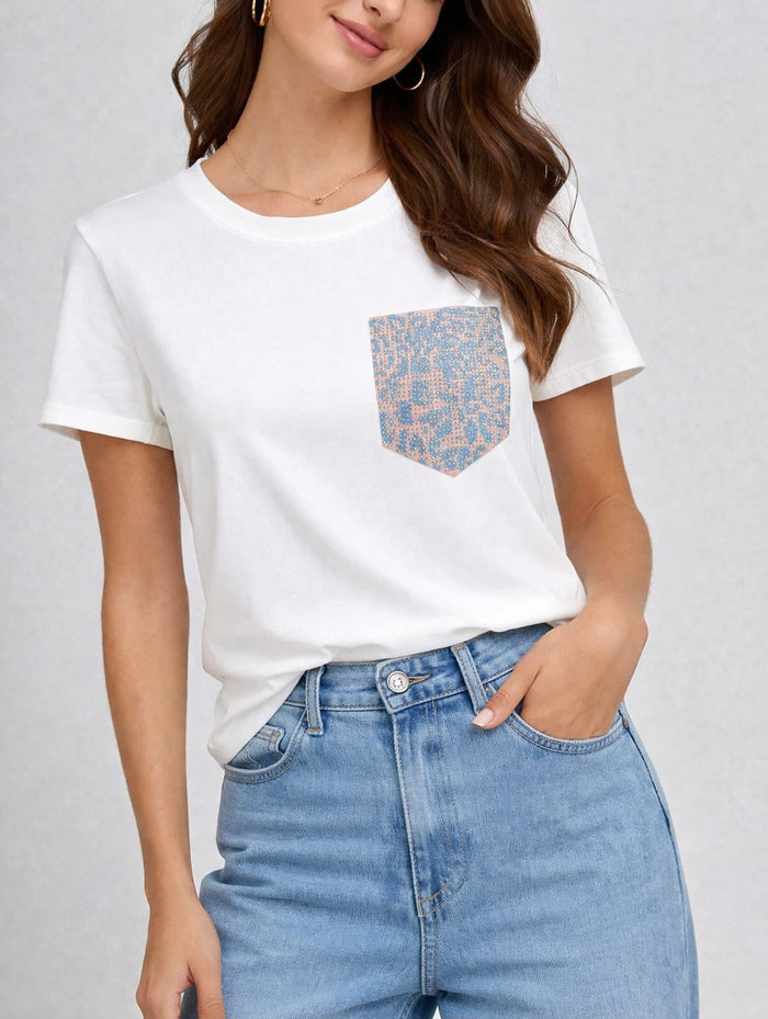 White short sleeve crewneck tee with a blue patterned chest pocket, styled with light-wash jeans.