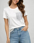 Woman wearing a white short sleeve crewneck t-shirt with a sparkling crystal-embellished pocket, styled with light wash jeans.