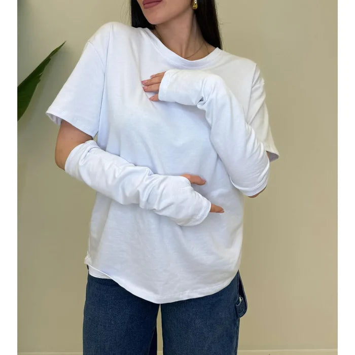 Woman wearing a clean white knit top with layered long sleeves and blue jeans.