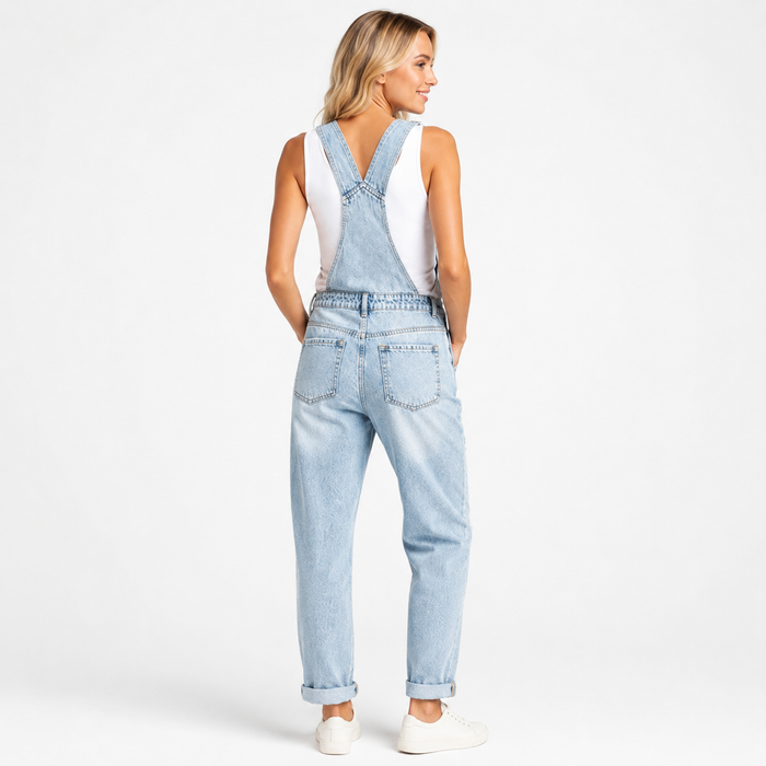 Women's light blue cropped denim overalls on a professional model, back view showing crossed straps, pockets and rolled hems.