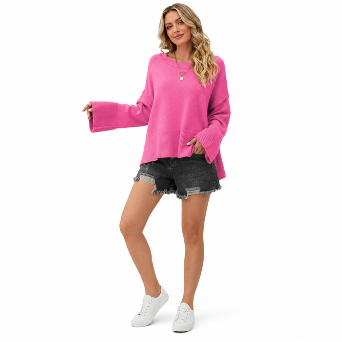 Women's pink dropped shoulder sweater with wide flare sleeves, ribbed hem and side slit styled with dark denim shorts on white