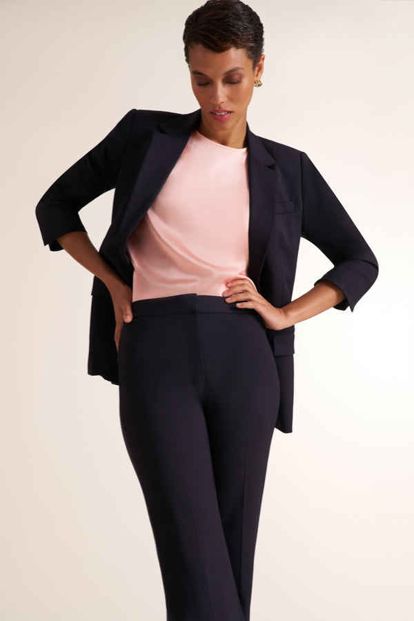A model posing in a black tailored blazer and matching trousers over a light pink top, set against a plain light beige studio background. | Exclude
